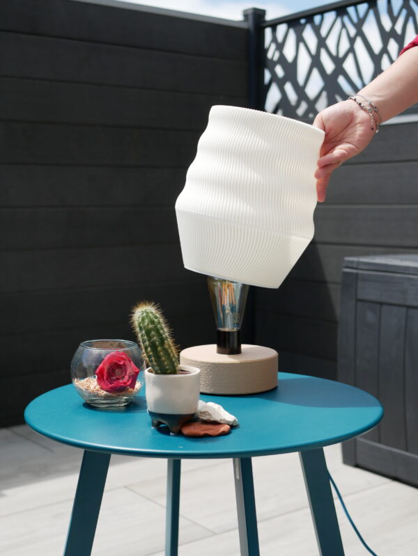 White lamp design and printed by homa kraft. The lamp is outside, turn off and use a lamp-base design by us. It's on a table with a cactus and other decorations