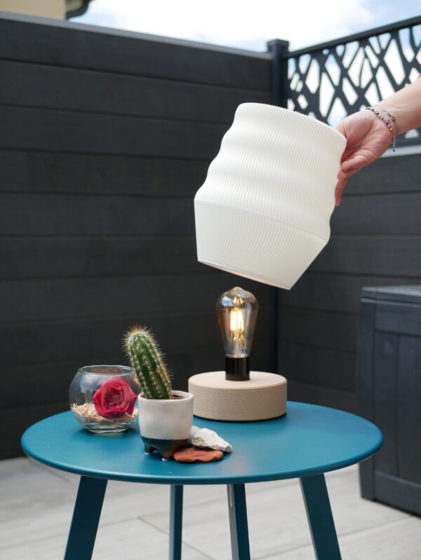 White lamp design and printed by homa kraft. The lamp is outside, turn on and use a lamp-base design by us. It's on a table with a cactus and other decorations